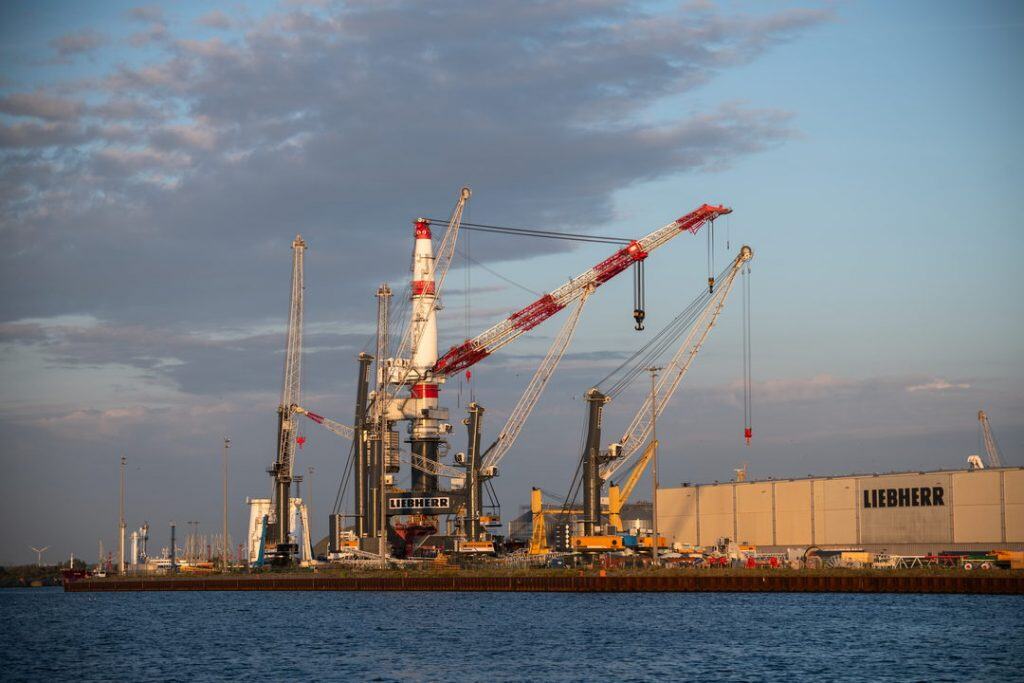 Große Kräne und Fabrik am Wasser im Hafen bei Sonnenuntergang.