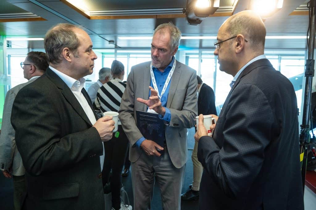 Drei Männer im Business-Dialog bei einer Konferenz in einem modernen Raum.