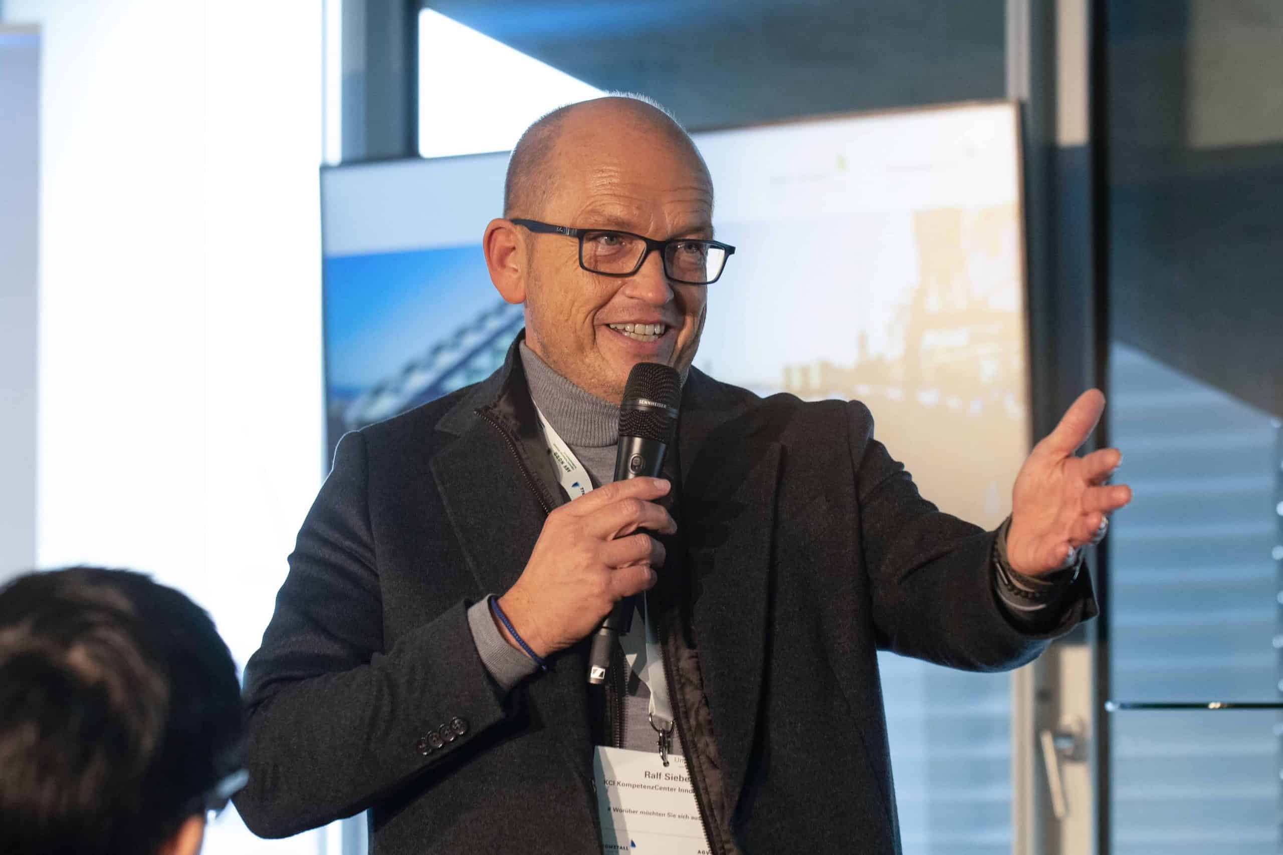 Mann hält Mikrofon und spricht bei einer Konferenz.