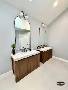 Bathroom with two wood vanities, white countertops, black fixtures, and freshly painted light gray walls