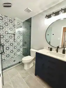 Remodeled bathroom with patterned shower tile, glass enclosure, and dark vanity with new light countertop