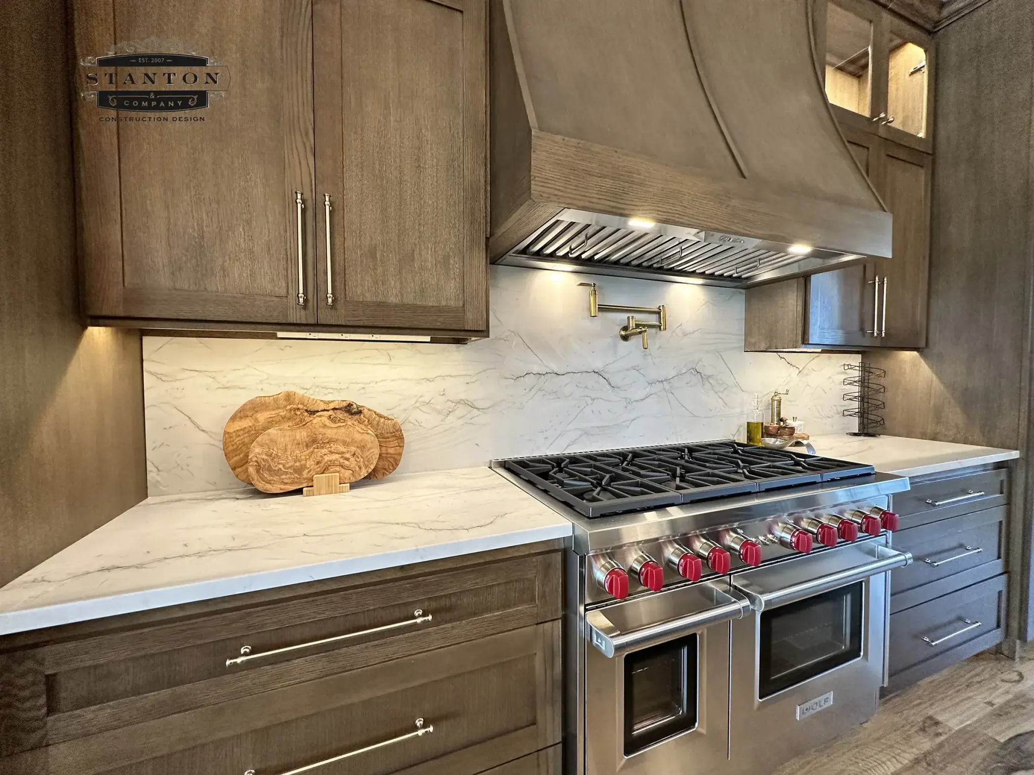 Kitchen with wood cabinetry, light countertops, matching stone-look backsplash, and stainless steel range