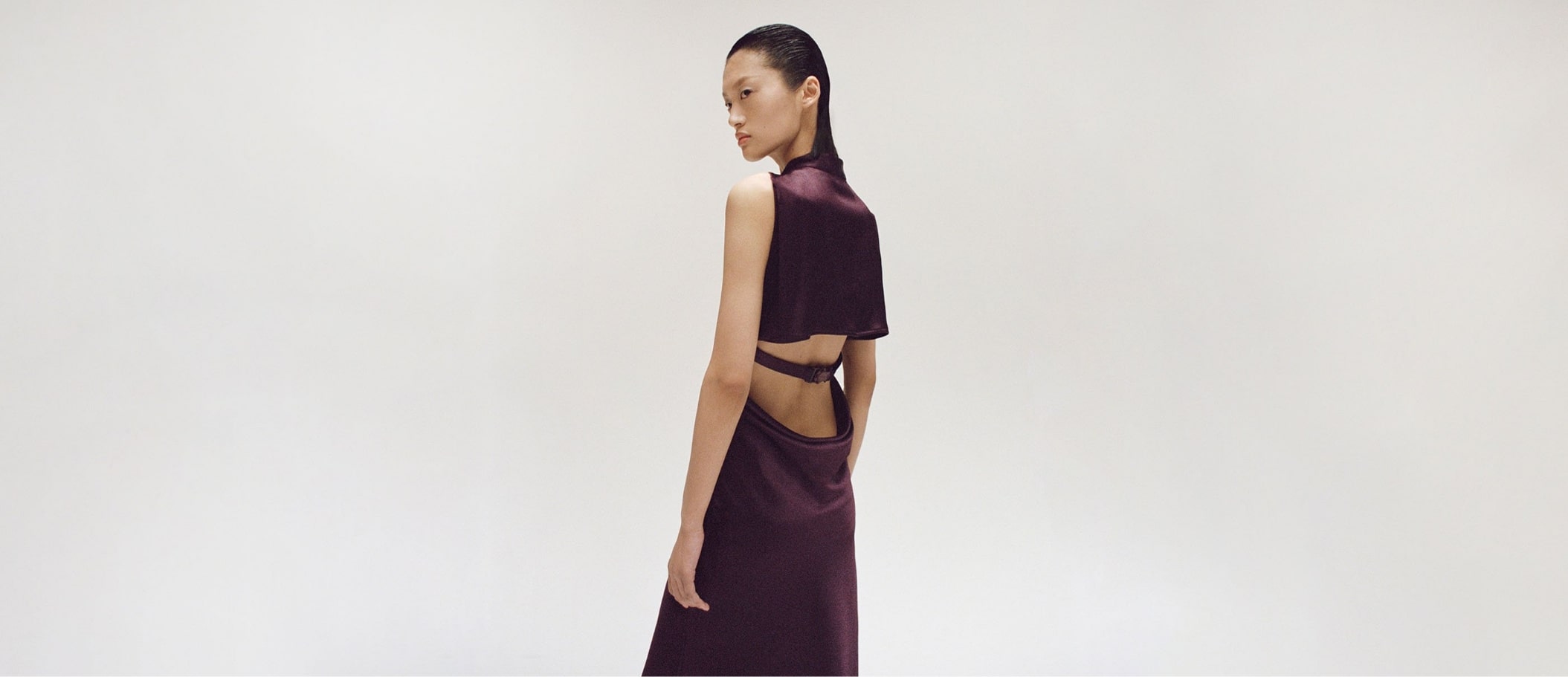 Elegante mulher vestida com roupa de alta costura em tom ameixa, em fundo minimalista.