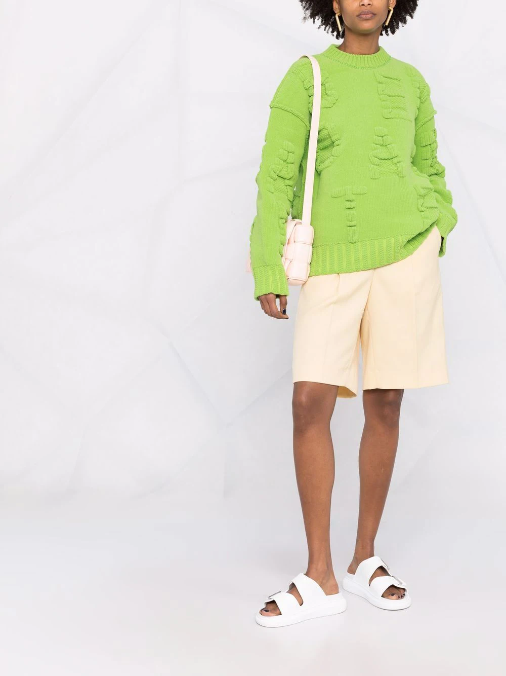 Conjunto de moda com suéter verde bright, calções bege e sandálias brancas com duas faixas.