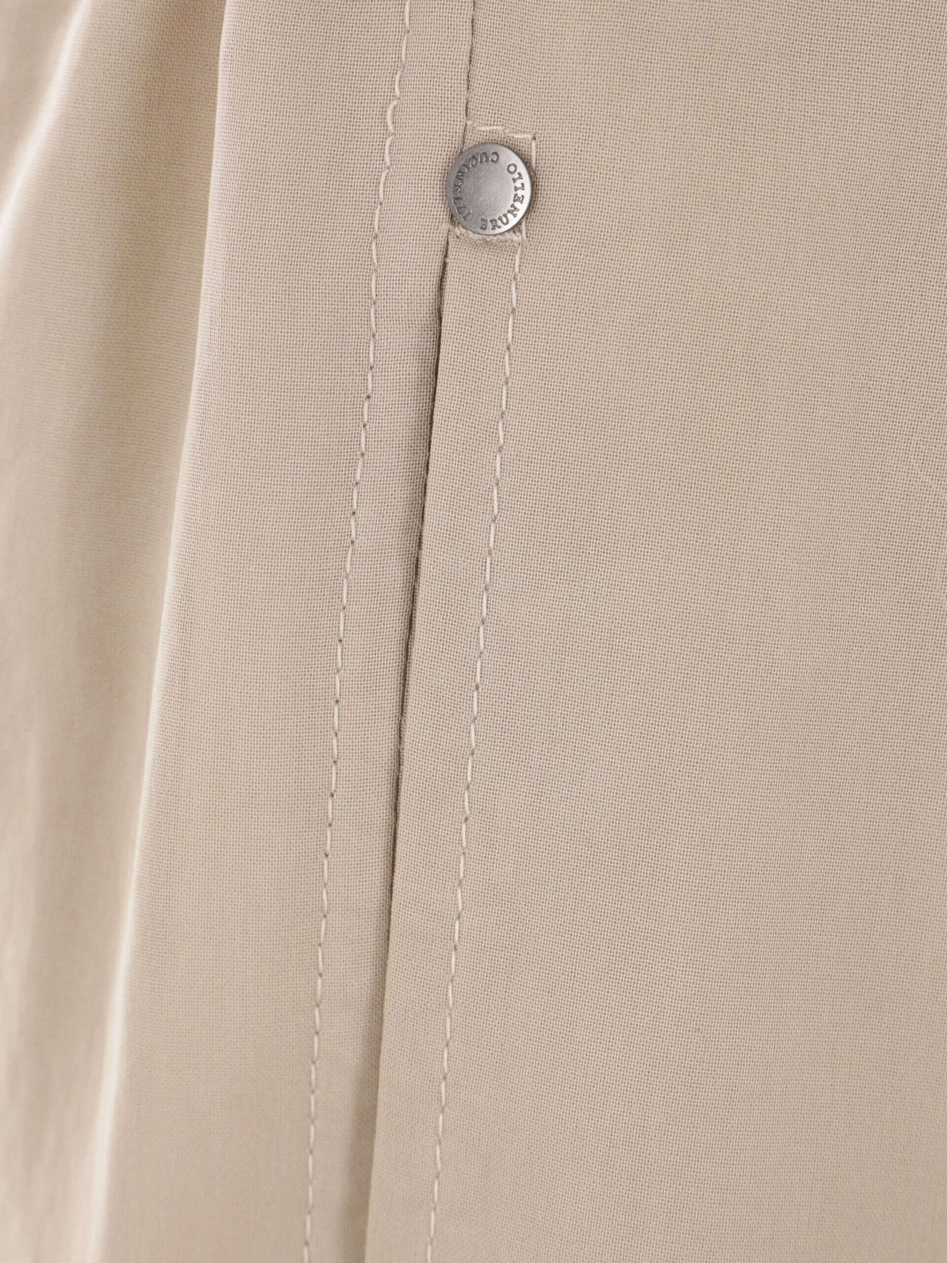 Botão de metal com detalhe de costura no vestido bege.