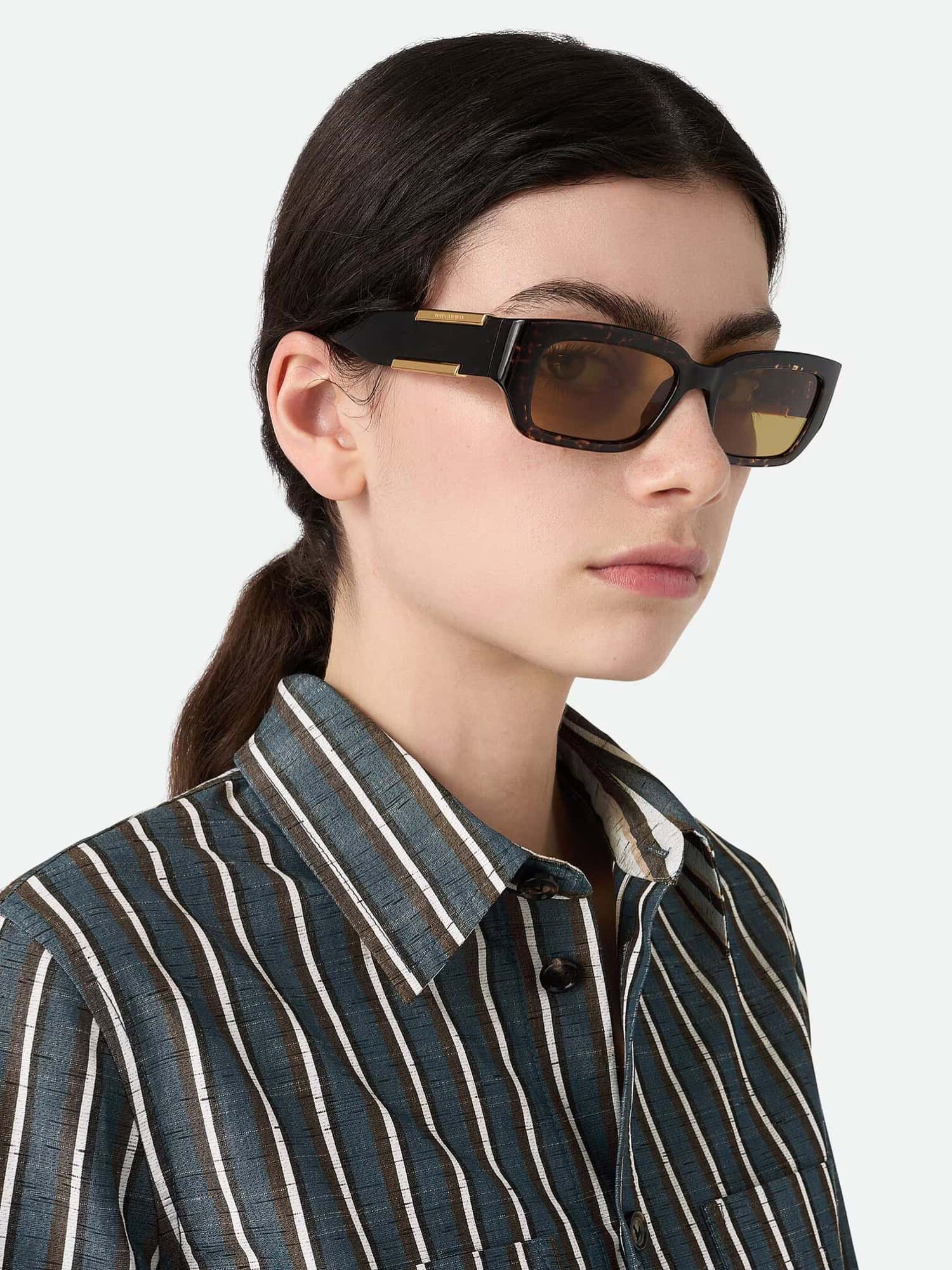 Moderna óculos de sol com armação escura e detalhes dourados para um look elegante.