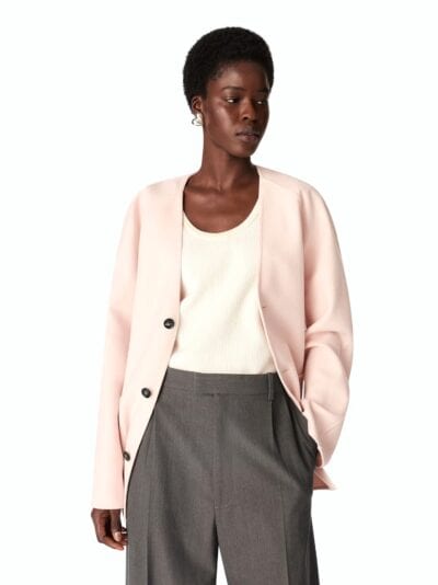 Elegante mulher com blazer rosa claro e calças cinzentas em estilo de moda feminina e masculina.