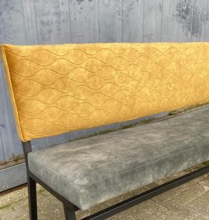 Alt tekst: Zwart metalen bank met gele, gestoffeerde rugleuning en zachte bekleding, geschikt voor interieurdecoratie.