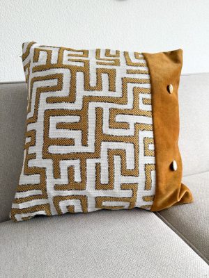 Geweven sierkussen met geometrisch patroon. Uniek decoratief kussen met goud en wit dessin en suède rand voor woonkamer.