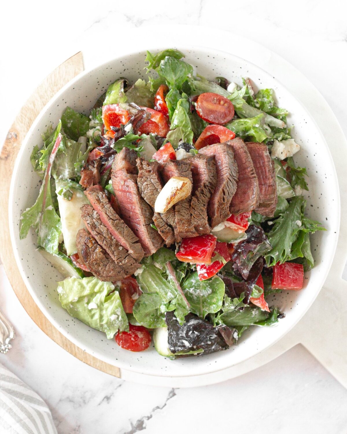 Beef Tenderloin with Garden Salad served in a shallow bowl and topped with a fried garlic clove.