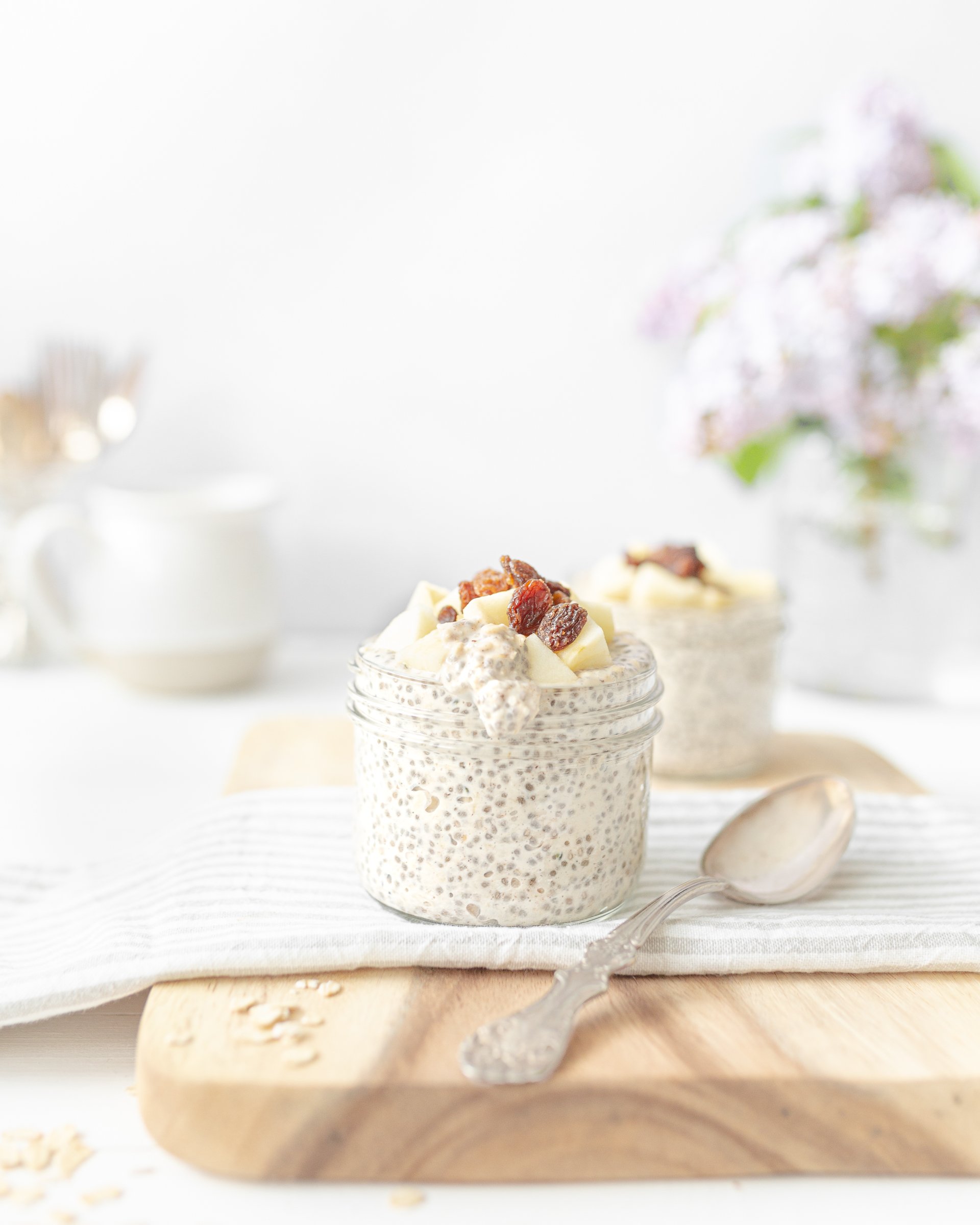 Cinnamon Raisin Overnight Oats portioned into two mason jars and topped with chopped apples and raisins. 