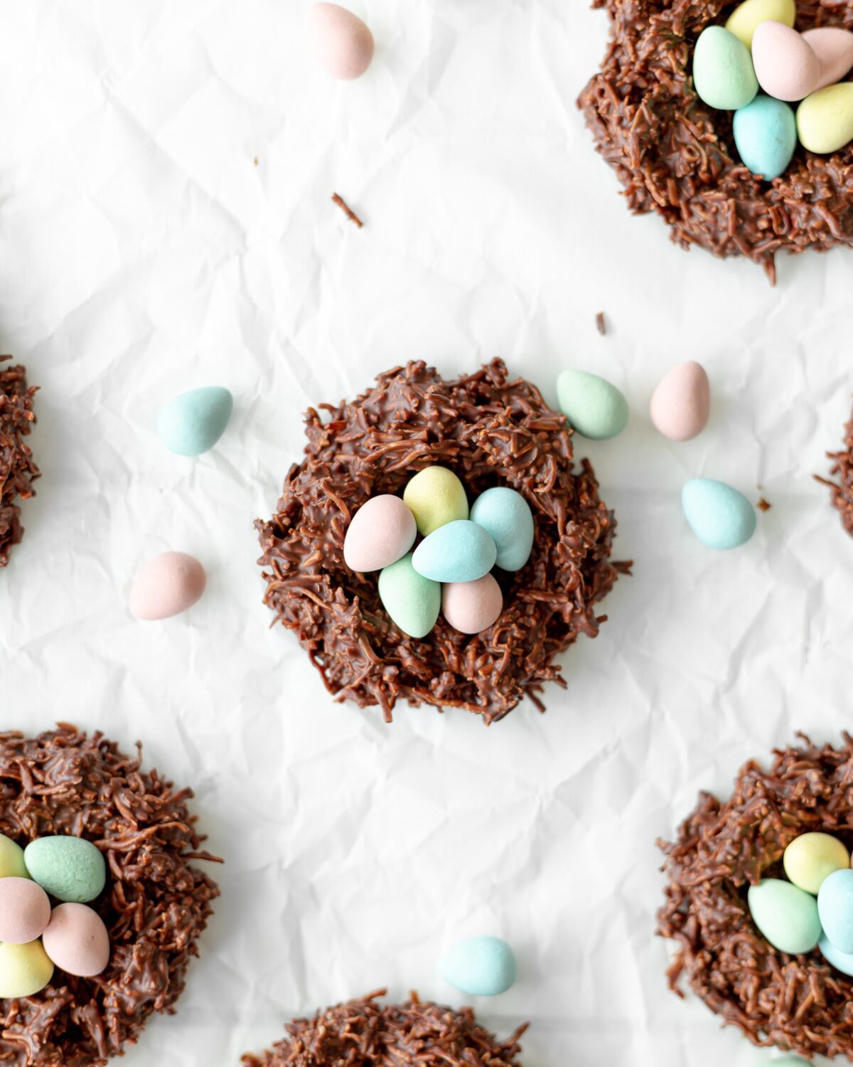 Chocolate Coconut Mini Egg Nests on parchment paper surrounded by mini eggs.