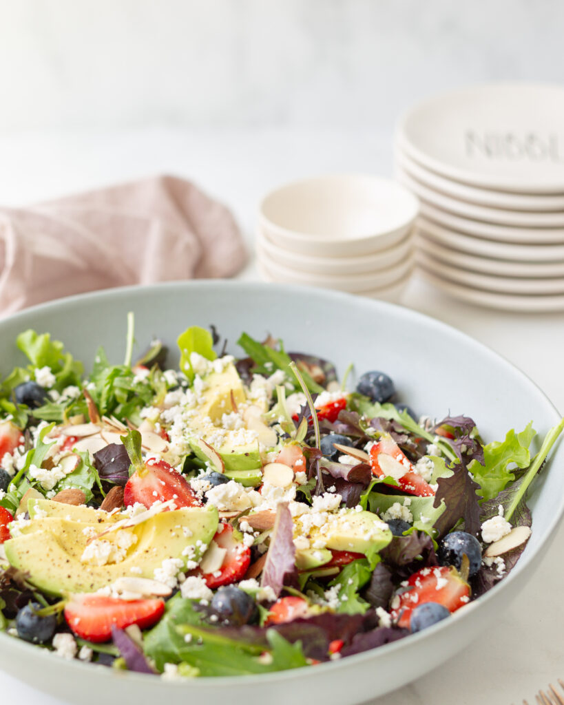 Green Salad with Berries and Avocado displayed in a large shallow bowl, very rustically.