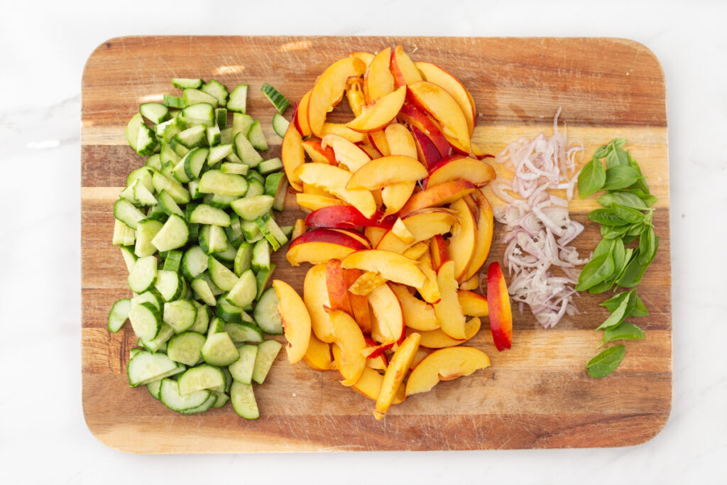 Process shot #1: Cucumbers, nectarines and shallots chopped on a cutting board and basil leaves picked.