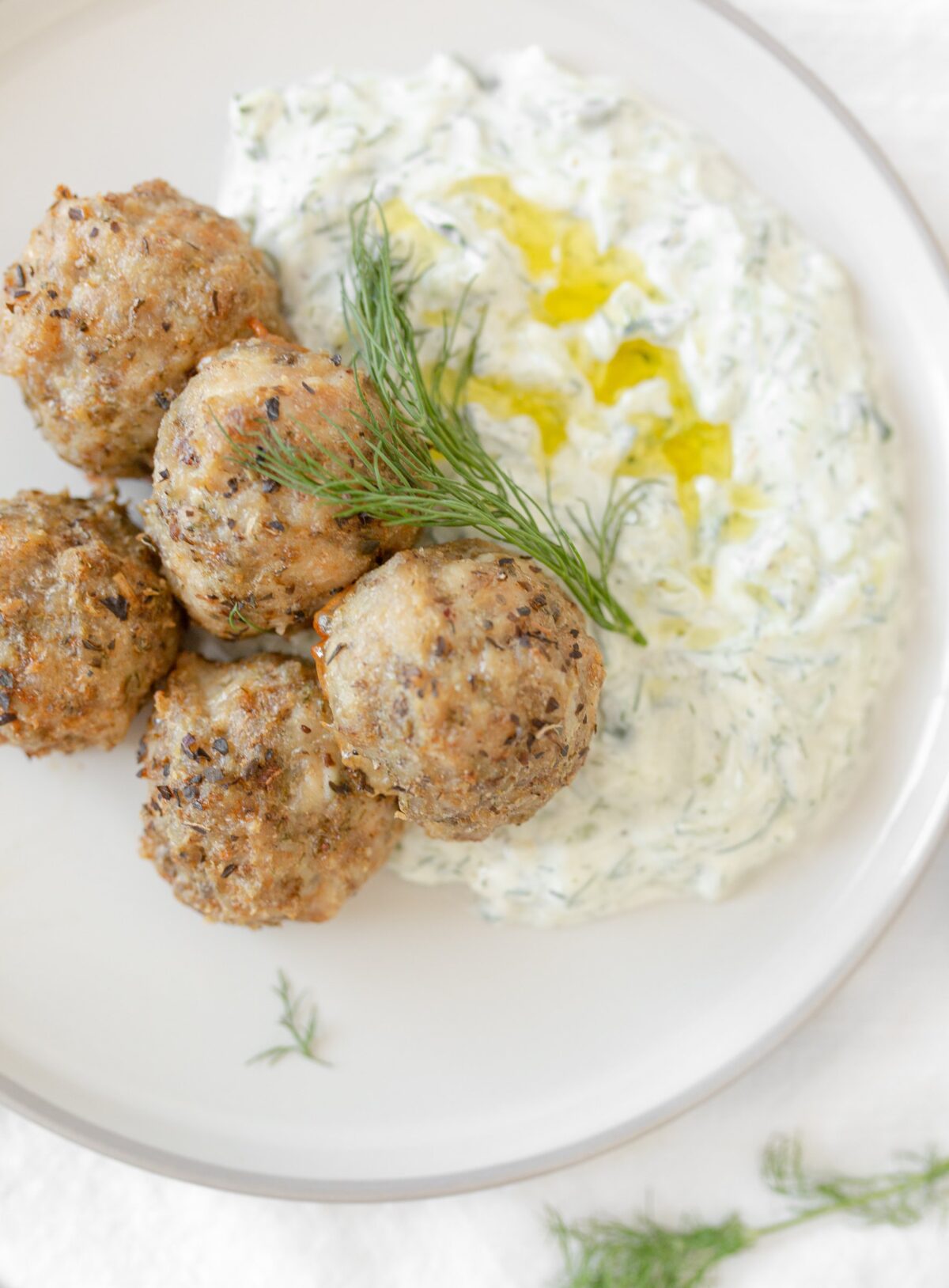 Greek-style Chicken Meatballs with Tzatzaiki plated and topped with fresh dill.