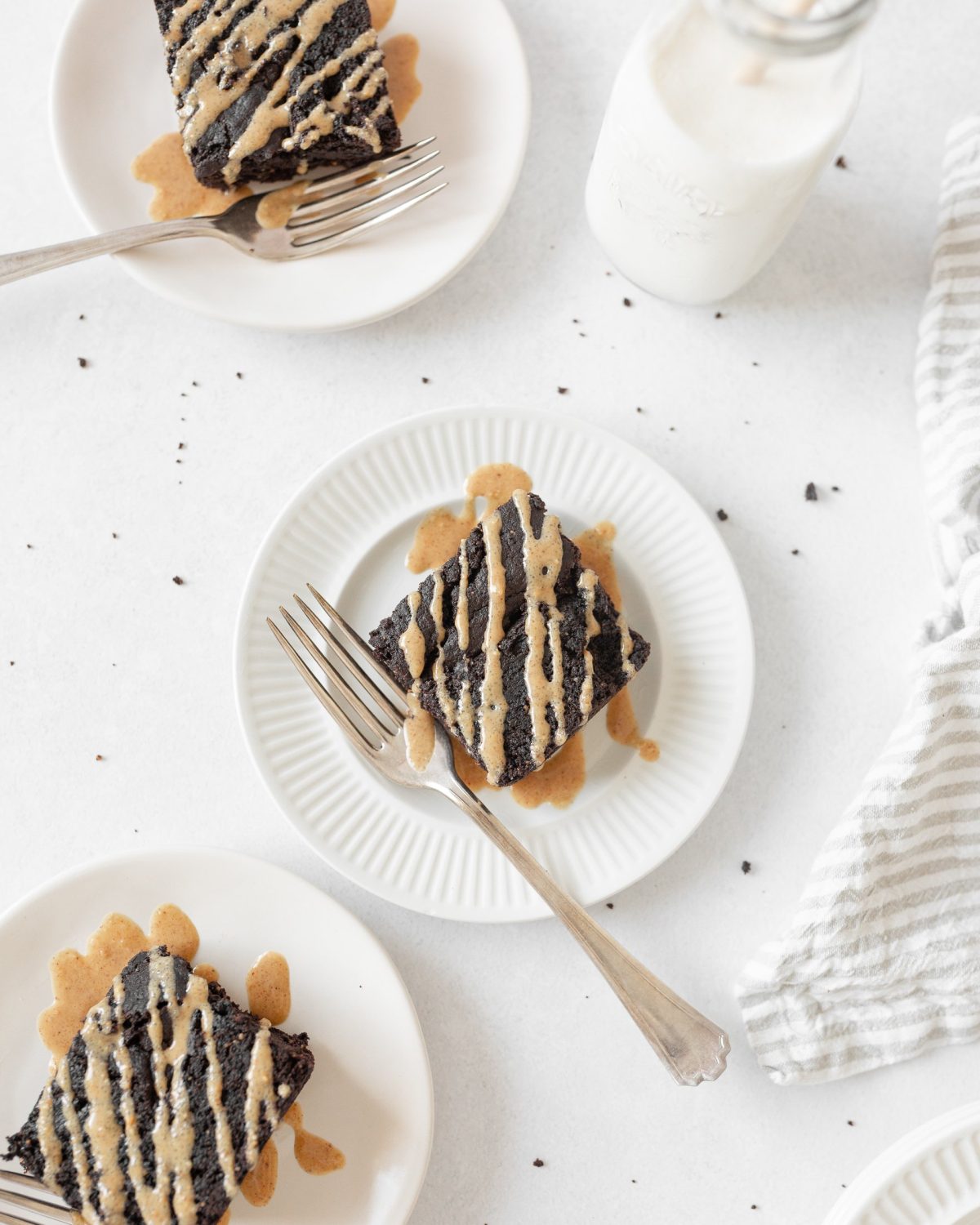 3 Flourless Peanut Butter Brownies on small plates, drizzled with peanut butter sauce.
