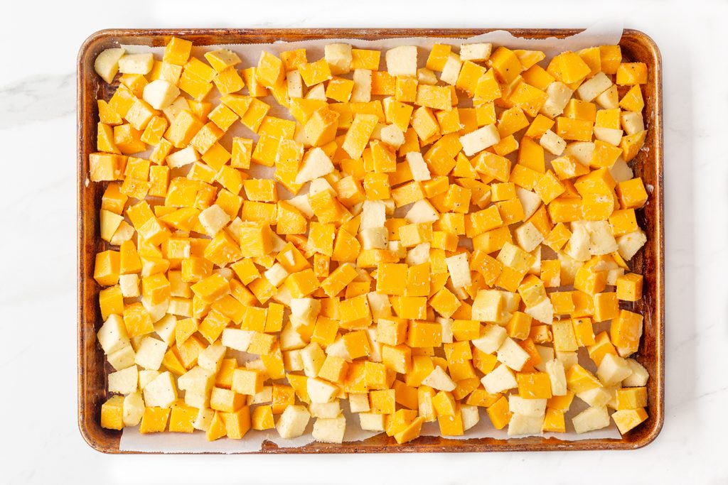 Process shot #1: chopped butternut squash and apple spread out on a parchment-lined baking sheet.