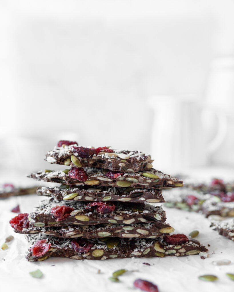 Chocolate Seed Bark with Cranberries broken up in pieces and stacked on top of each other on parchment paper.