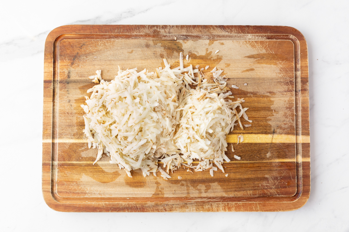 Process shot #1: Russet potatoes shredded on a wooden cutting board.
