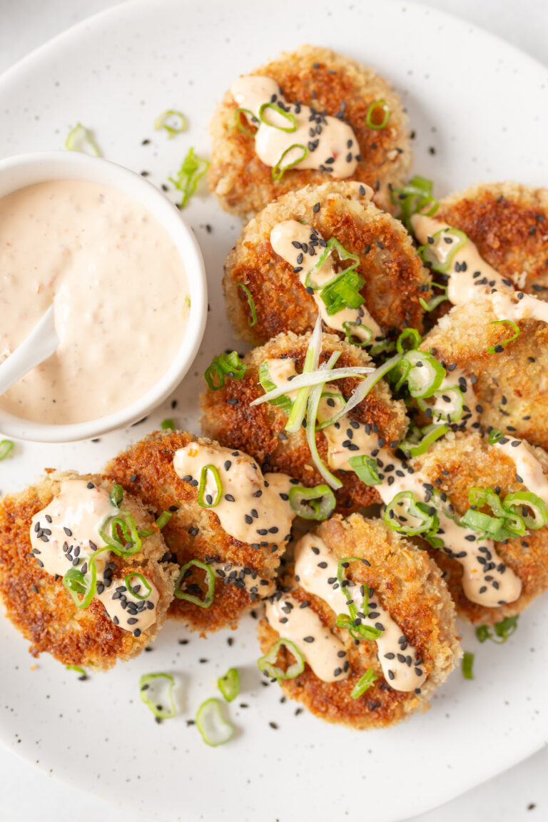 Asian-style Tuna Cakes plated and topped with spicy mayo, green onions and black sesame seeds.