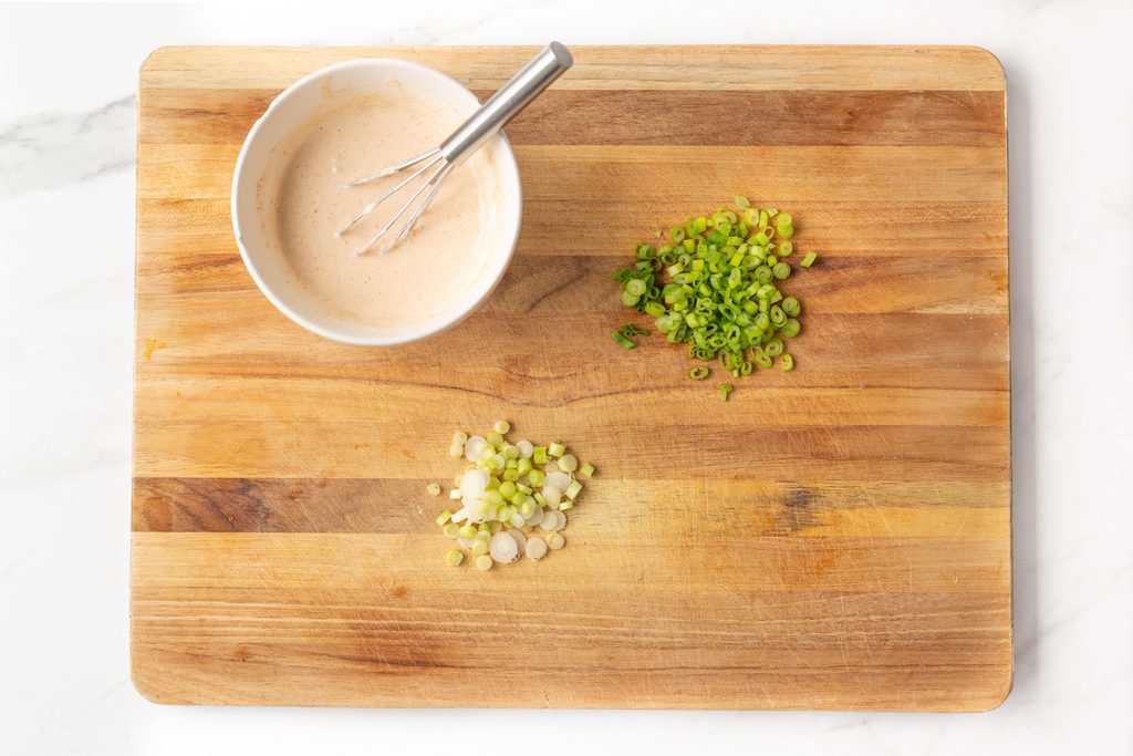 Process shot #1: chopped green onions, whites and greens separated on a cutting board. Spicy mayo whisked together in a small bowl.