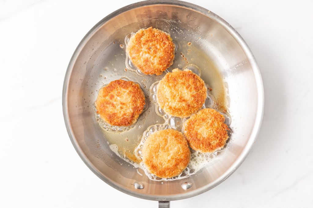 Process shot #4: Tuna cakes fried until golden brown and crispy in a stainless steel frying pan.
