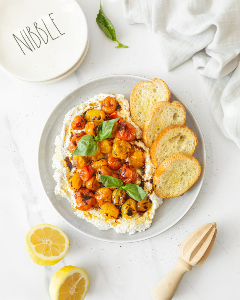 Whipped ricotta with roasted tomatoes and basil plated and served with crostinis. 