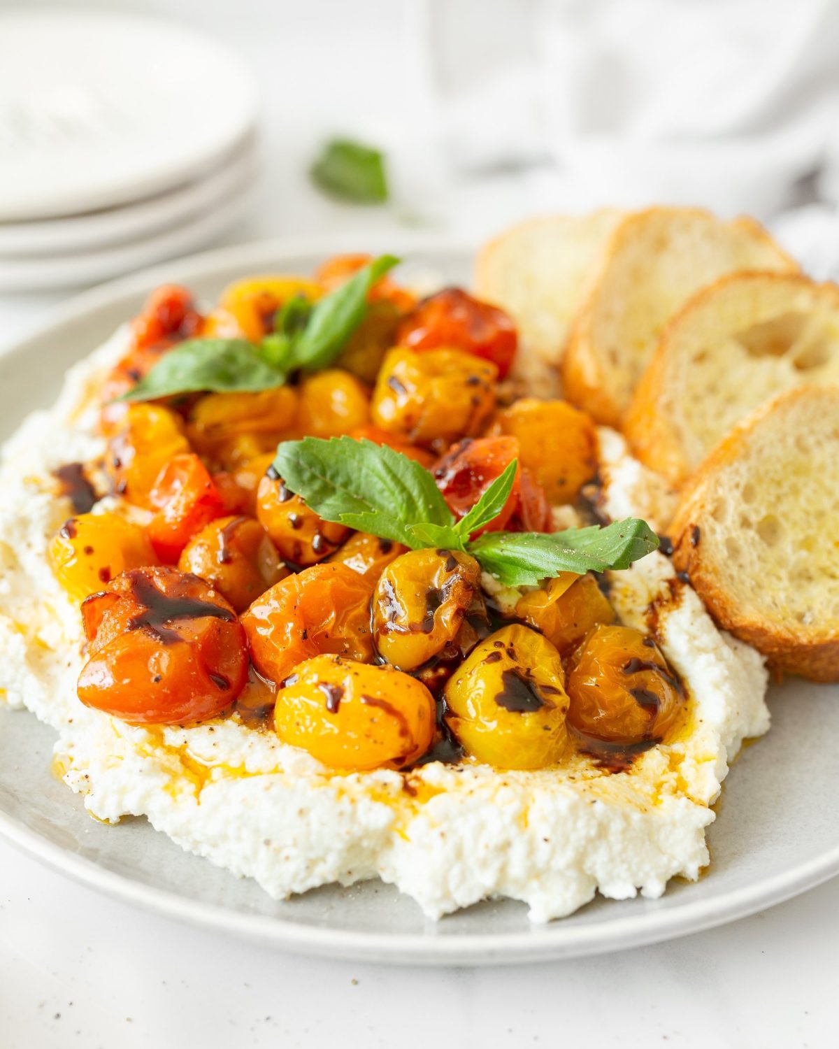 Whipped Ricotta with tomatoes plated and garnished with balsamic reduction and basil.