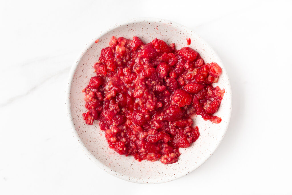 Process shot #2: Fresh raspberries roughly mashed on a small plate.