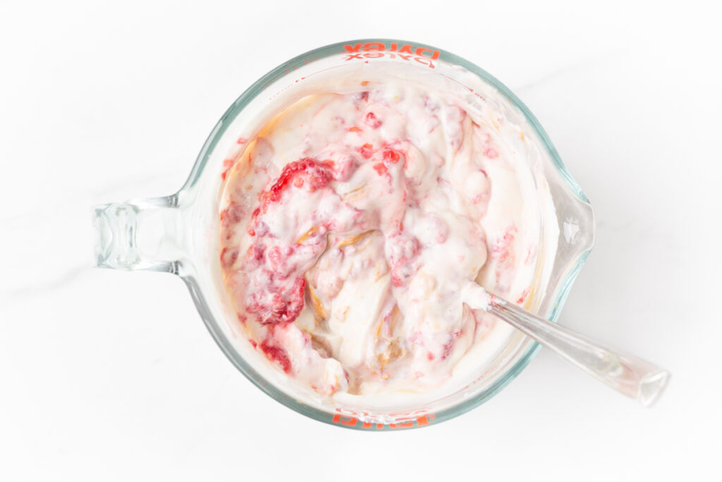 Process shot #3: greek yogurt, honey, peanut butter and raspberries partially mixed in a large glass measuring cup.