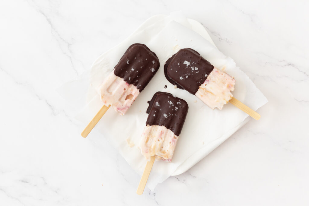 Process shot #6: Peanut Butter and Jam Frozen Yogurt Bars coated in chocolate and placed on a parchment-lined plate and garnished with flakey sea salt.