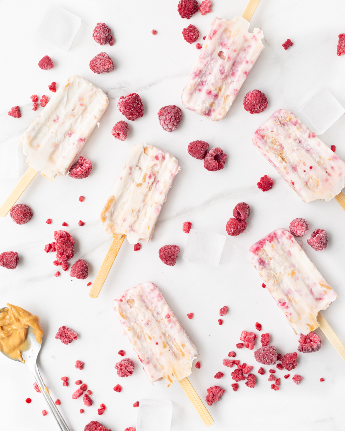 Peanut Butter and Jam Frozen Yogurt Bars spread out on a marble slab, surrounded by frozen raspberries.