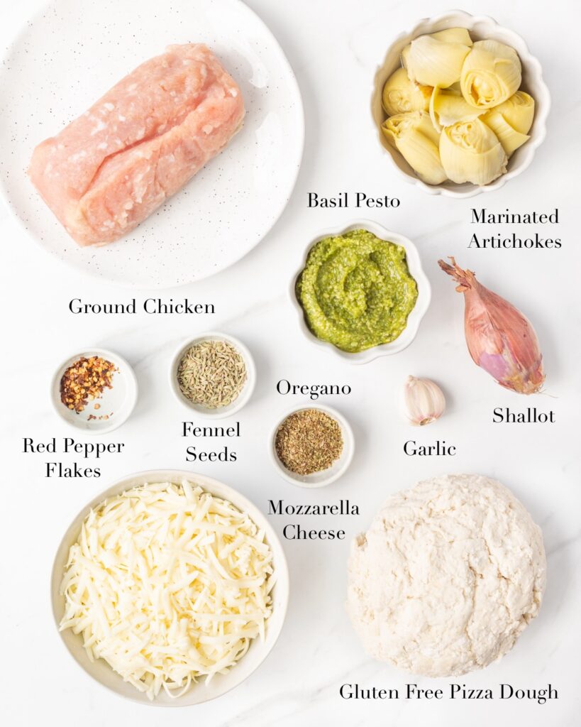 Ingredients for Ground Chicken Pizza with Pesto and Artichokes portioned out on a marble slab.