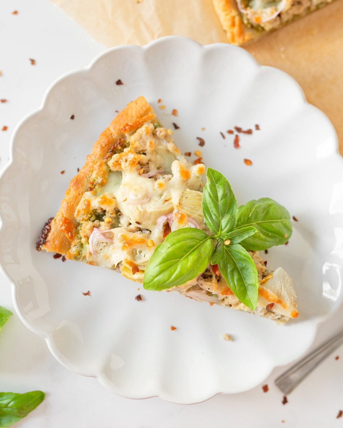 A slice of pesto chicken pizza on a plate with fresh basil on it.
