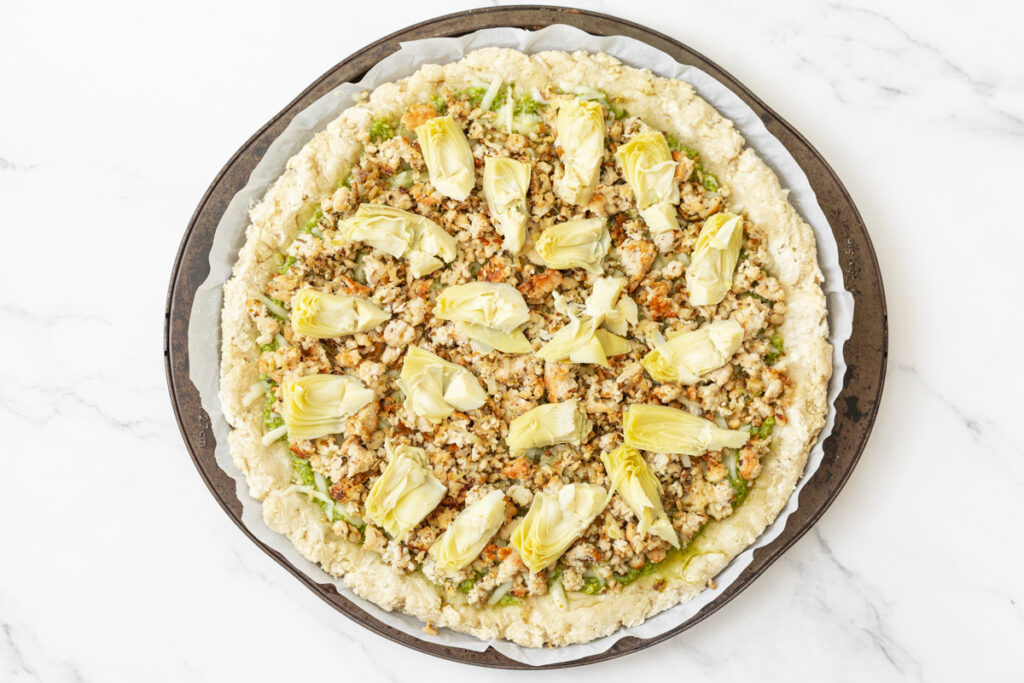 Process shot #3: Toppings added to the pizza crust including mozzarella cheese, the cooked chicken and shallots mixture and the artichoke hearts.