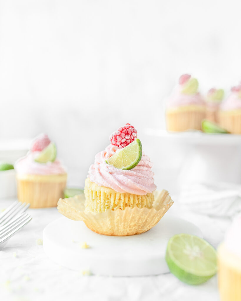Key Lime Cupcakes topped with raspberry frosting and garnished with a small slice of key lime and a frozen raspberry.