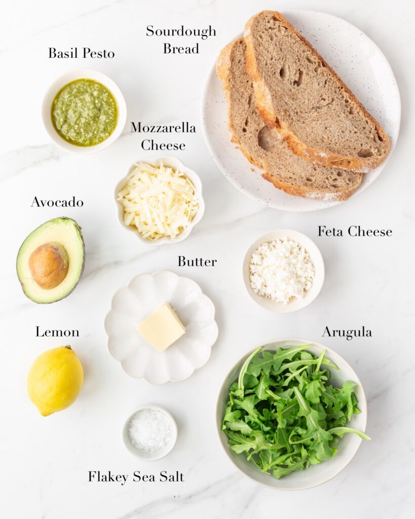 Ingredients for Grilled Pesto Avocado and Feta Sandwich portioned out on a marble slab.