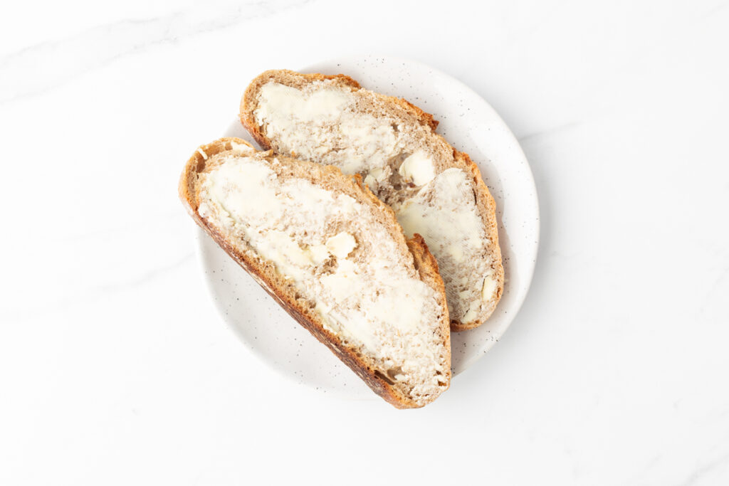 Process shot #1: Sourdough bread slices buttered on a plate.