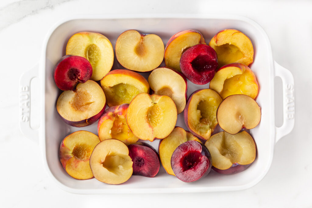Process shot #1: Fresh peaches and black plums cut in half, pitted and arranged in a rectangular baking dish.