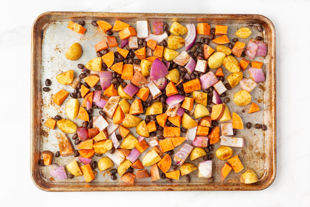Process shot #1: Chopped yams, potatoes and purple onion tossed in olive oil and spices along with black beans on a baking sheet.