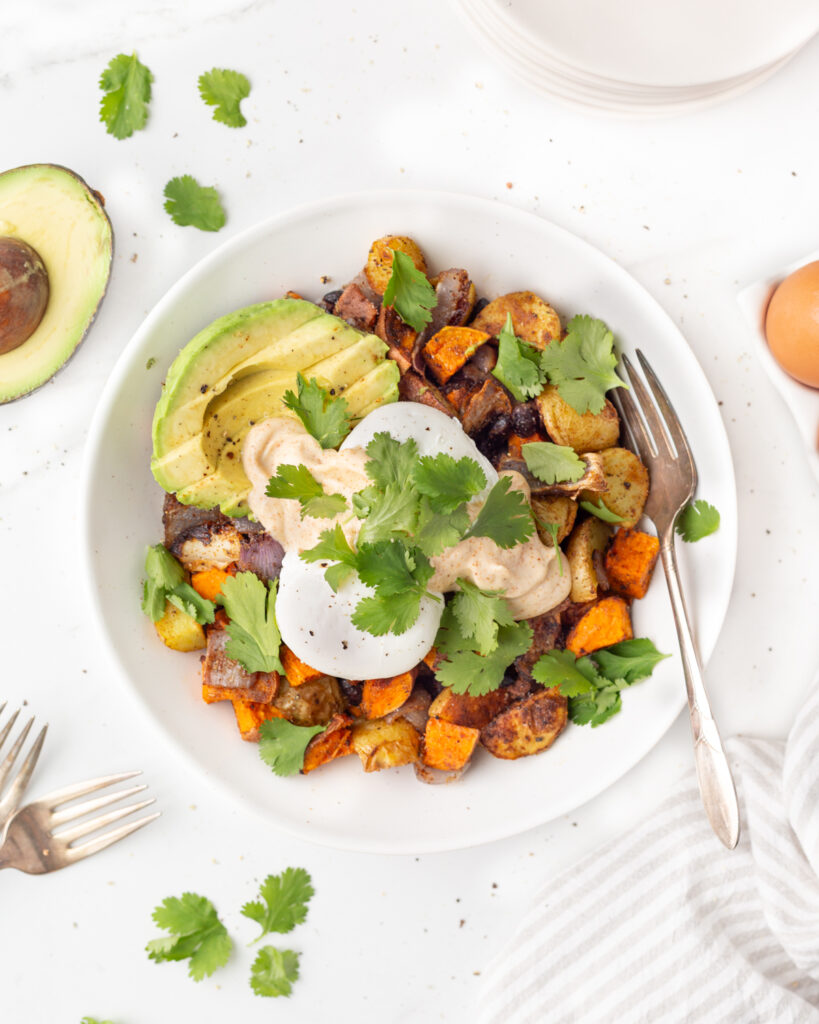 Southwest Breakfast Bowl plated with roasted potatoes, sliced avocado, poached eggs and garnished with fresh cilantro.