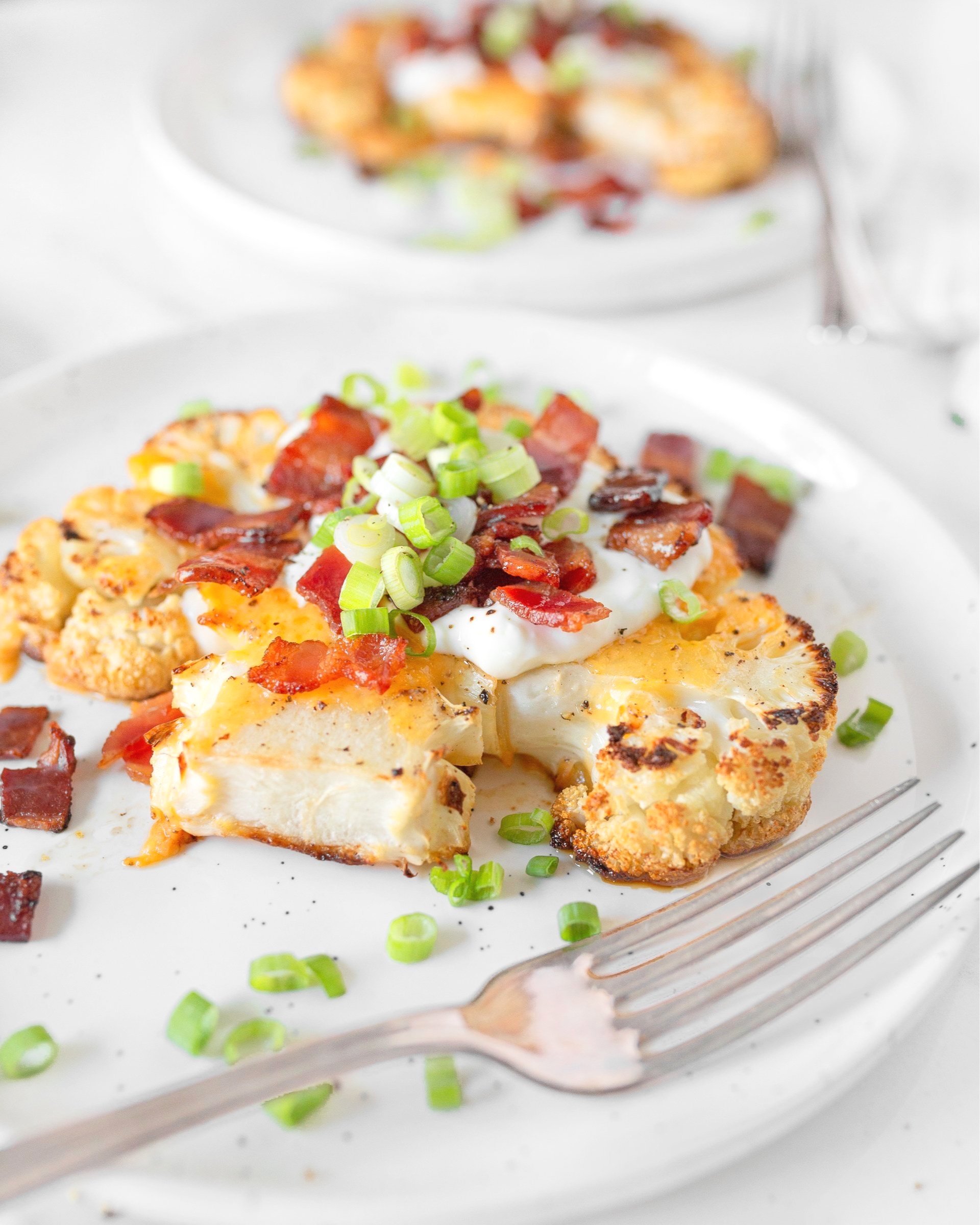 Loaded Baked Cauliflower Steaks plated and garnished with bacon and sliced green onions. 