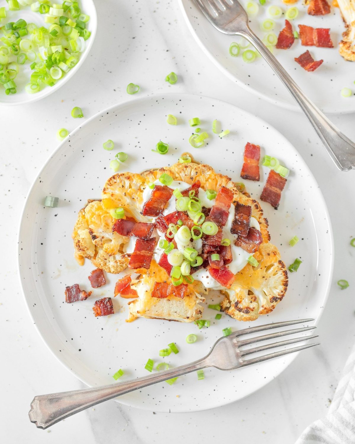 Loaded Baked Cauliflower Steaks plated and topped with green onions.
