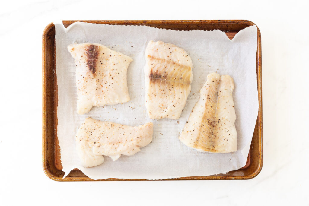 Process shot #1: Cooked cod fillets on a parchment-lined baking sheet. 