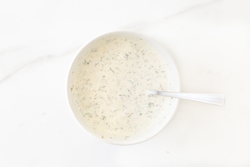 Process shot #2: Homemade tartar sauce mixed in a small white bowl with a fork. 