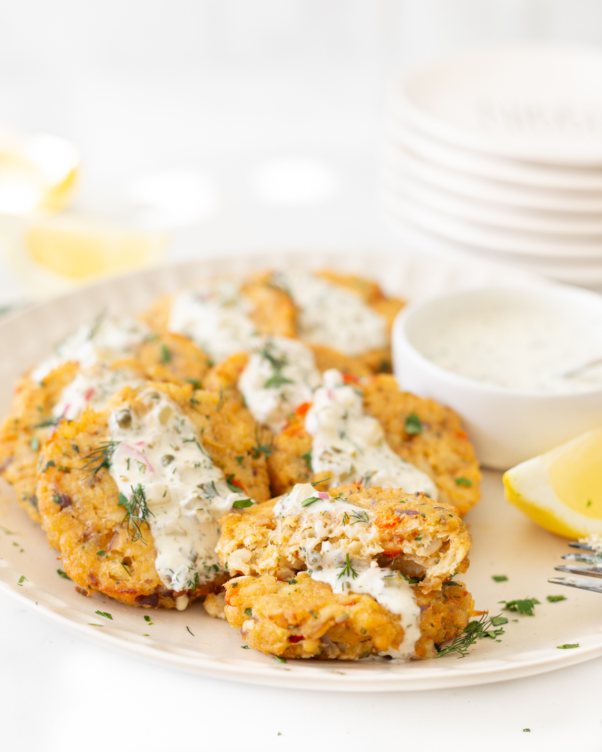 Air Fryer Cod Cakes plated and topped with tartar sauce. One is cut in half and stacked on top of itself. 