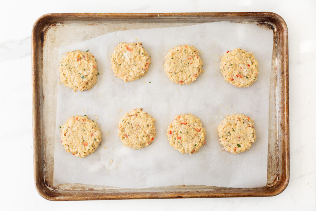 Process shot #4: 8 cod cakes on a parchment-lined baking sheet ready to be air-fried in the oven. 