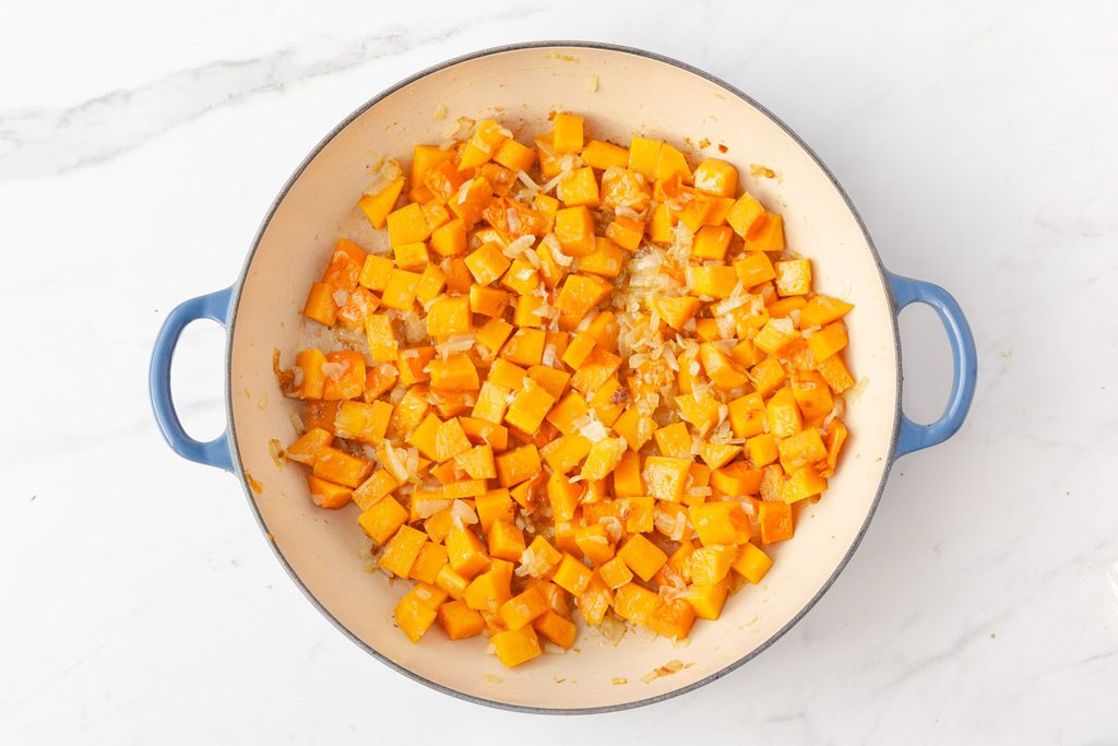 Process shot #1: An enamelled cast iron skillet with sautéed onion, garlic and butternut squash in it.
