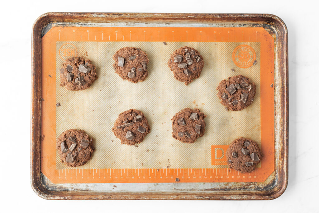 Process shot #4: Gluten Free Double Chocolate Cookies dough scooped onto a silicone-lined baking sheet and topped with extra chocolate chunks.