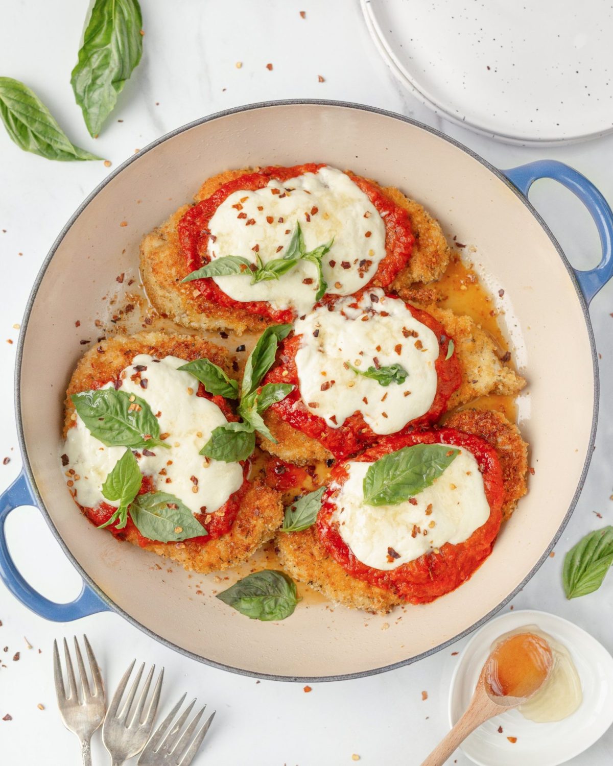 Chicken Parmigiana with Burrata and Honey cooked in a skillet and topped with fresh basil.